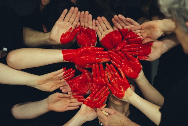 Hands placed together with red paint that forms a heart