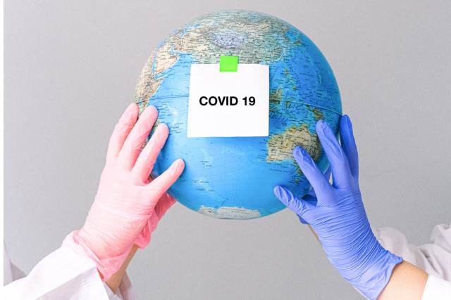 Hands with gloves holding a globe with "COVID 19" taped on the front of it